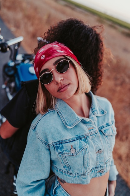 Selbstbewusste blonde Frau, die ein Denim-Outfit trägt und mit ihrem Partner auf einem Motorrad posiert