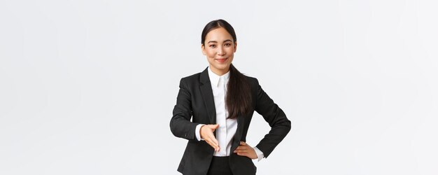 Selbstbewusste, erfolgreiche Geschäftsfrau im schwarzen Anzug streckt die Hand zum Handshake-Gruß-Geschäftspartner mit erfreutem, entschlossenem Lächeln aus, das bereit ist, den Vertrag auf weißem Hintergrund zu unterzeichnen