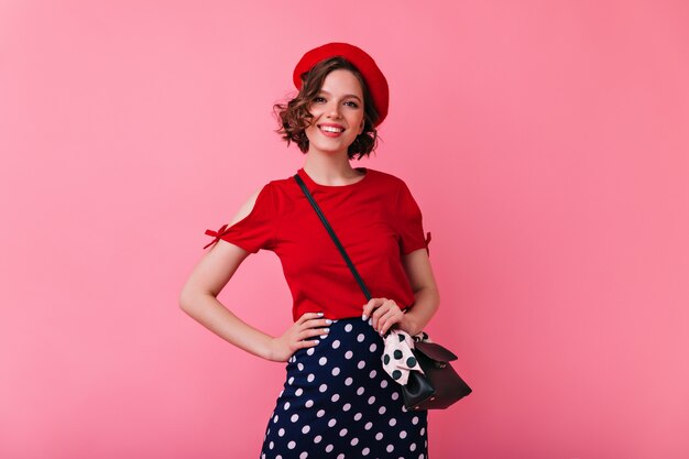 Selbstbewusste Französin posiert mit aufrichtigem Lächeln. Romantische kaukasische Frau in der roten Baskenmütze, die positive Gefühle ausdrückt.