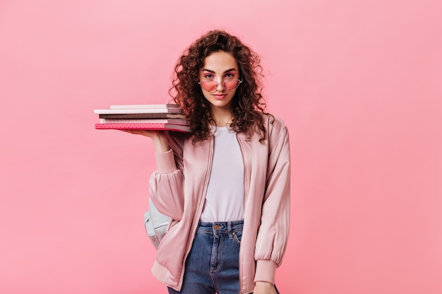Selbstbewusste Frau im täglichen Mode-Outfit, das Bücher auf rosa Hintergrund hält