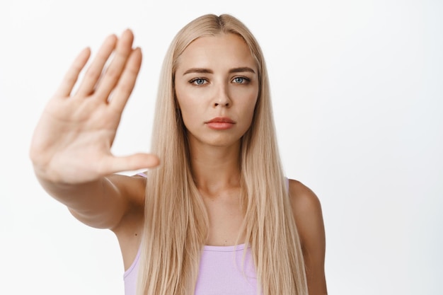 Selbstbewusste junge Frau streckt die Hand aus, um eine Stopp-Geste zu zeigen, die sagt, dass etwas nicht verboten ist, das auf weißem Hintergrund steht