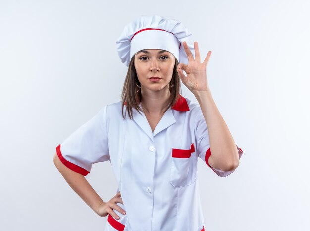 Selbstbewusste junge Köchin in Kochuniform, die eine gute Geste zeigt, die auf weißem Hintergrund isoliert ist