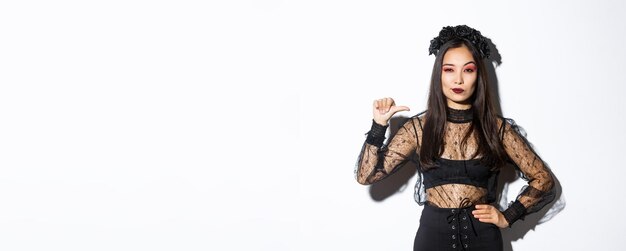 Selbstbewusste, stilvolle asiatische Frau, die entschlossen aussieht und schwarzes Spitzenkleid für Halloween-Party-Pointi trägt