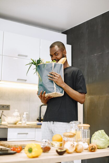 Selbstbewusster afrikanischer Hipster-Blogger, der Vlog über das Kochen auf Digitalkamera aufnimmt, sitzt in einer Küche