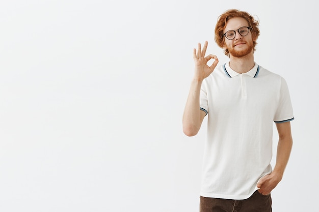 Selbstbewusster bärtiger Rotschopf, der mit Brille gegen die weiße Wand aufwirft