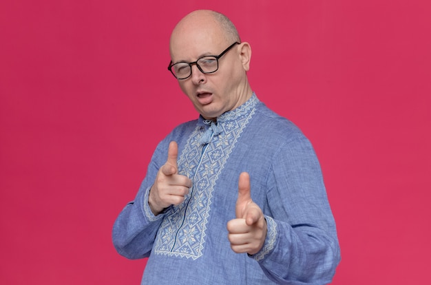 Selbstbewusster erwachsener Mann im blauen Hemd mit Brille, der mit den Augen blinzelt und nach vorne zeigt