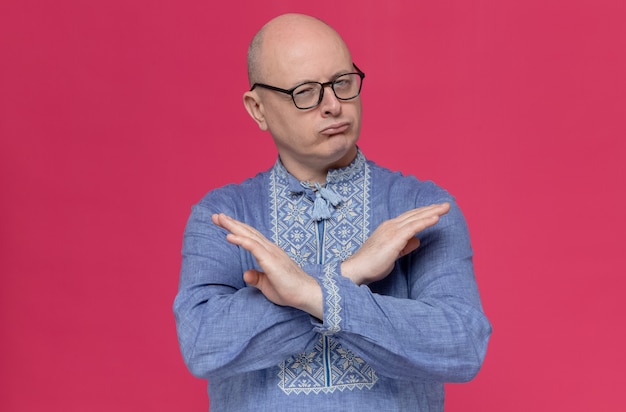 Selbstbewusster erwachsener slawischer mann in blauem hemd mit optischer brille, der seine hände kreuzt und kein zeichen gestikuliert