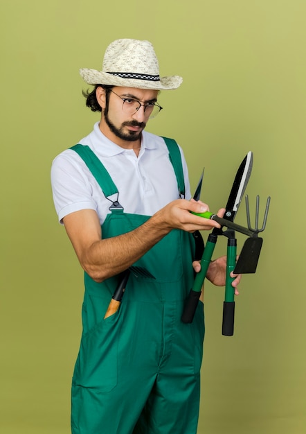 Selbstbewusster Gärtnermann in optischer Brille mit Gartenhut hält Schermaschinen