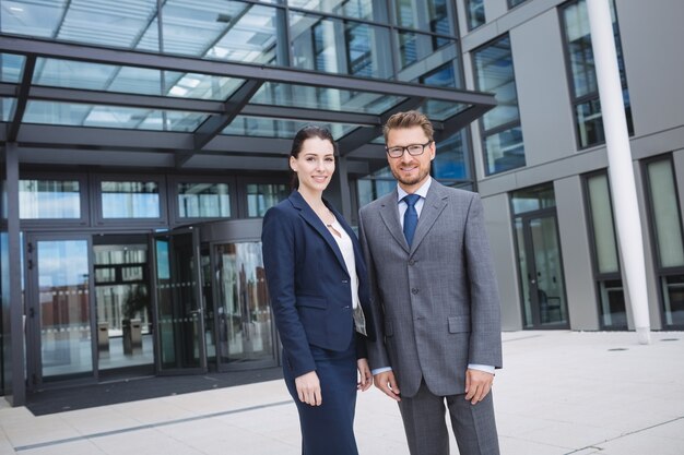 Selbstbewusster Geschäftsmann mit dem Kollegen, der außerhalb des Bürogebäudes steht