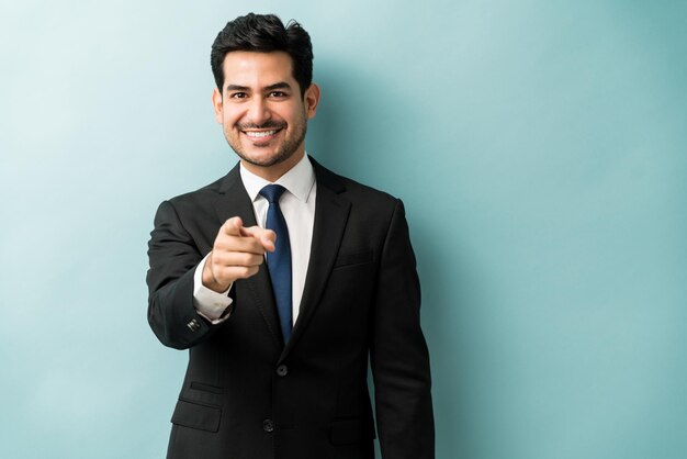 Selbstbewusster, gut aussehender junger Geschäftsmann, der mit dem Finger zeigt, während er vor isoliertem Hintergrund steht