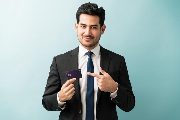 Selbstbewusster, gut aussehender männlicher Unternehmer, der auf seine Kreditkarte vor isoliertem Hintergrund zeigt
