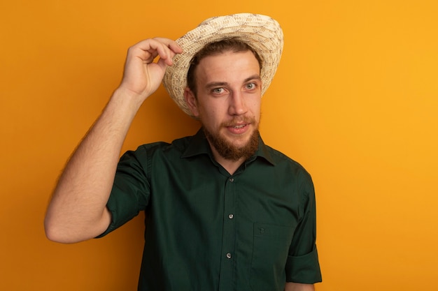 Kostenloses Foto selbstbewusster hübscher blonder mann mit strandhut schaut vorne isoliert auf orange wand