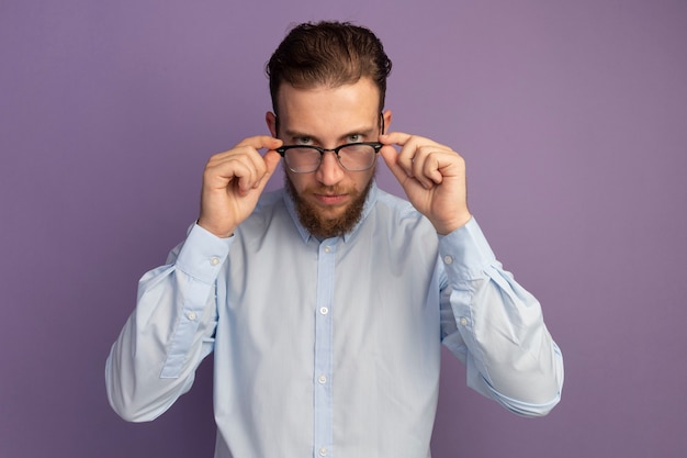 Selbstbewusster hübscher blonder Mann schaut durch optische Brille isoliert