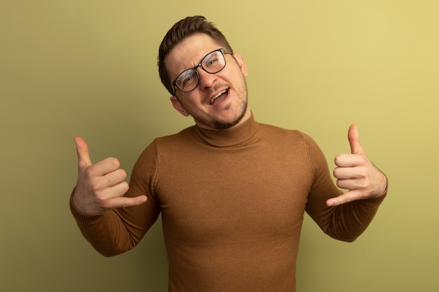 Selbstbewusster junger blonder gutaussehender Mann mit Brille, der eine lose Geste isoliert auf olivgrüner Wand macht