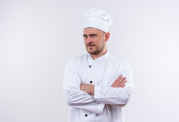 Selbstbewusster junger gutaussehender Koch in Kochuniform, der mit geschlossener Haltung isoliert auf weißer Wand steht