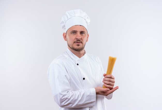 Selbstbewusster junger gutaussehender Koch in Kochuniform mit Spaghetti isoliert auf weißer Wand