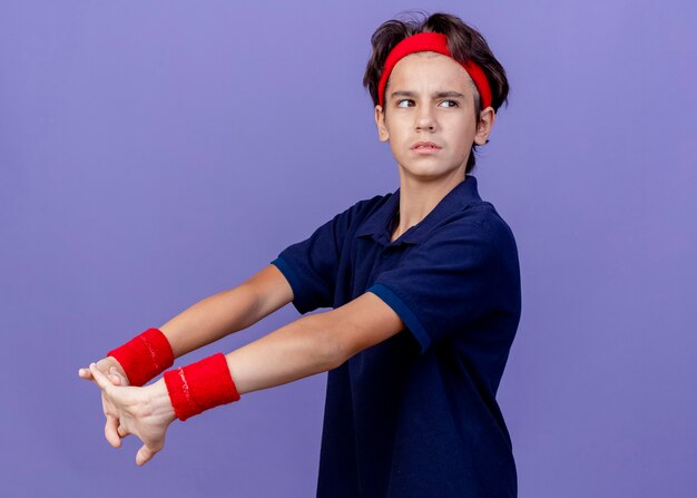 Selbstbewusster junger hübscher sportlicher Junge, der Stirnband und Armbänder trägt und Hände streckt