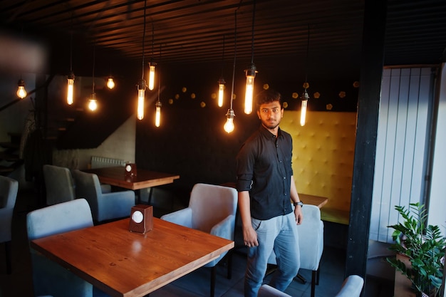 Selbstbewusster junger Inder im schwarzen Hemd, der im Café steht