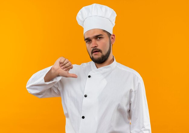 Selbstbewusster junger männlicher Koch in Kochuniform, der auf sich selbst zeigt, isoliert auf oranger Wand