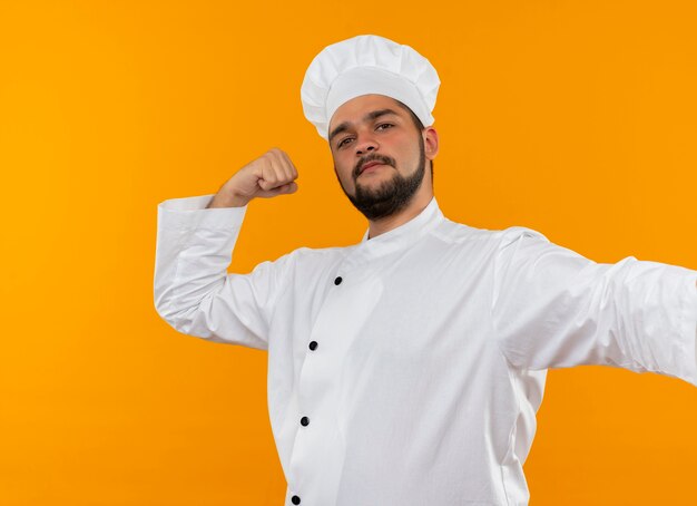 Selbstbewusster junger männlicher Koch in Kochuniform, der stark isoliert auf orangefarbener Wand gestikuliert