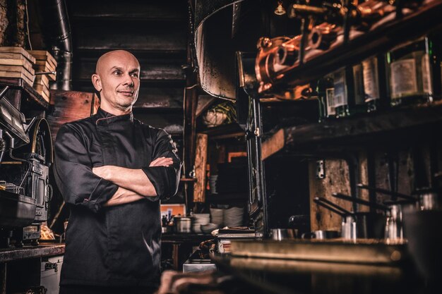 Selbstbewusster Koch in Uniform, der mit verschränkten Armen posiert und in einer Restaurantküche wegschaut.