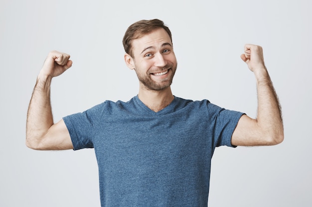 Selbstbewusster lächelnder Mann, der im Fitnessstudio trainiert, starken Bizeps beugt, Muskeln zeigt