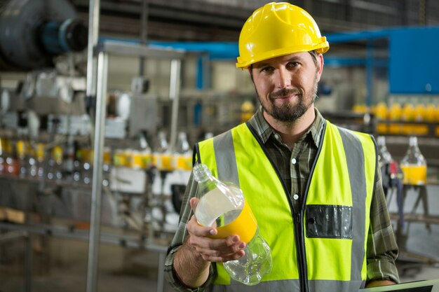 Selbstbewusster männlicher Arbeiter, der Flaschen in der Saftfabrik inspiziert