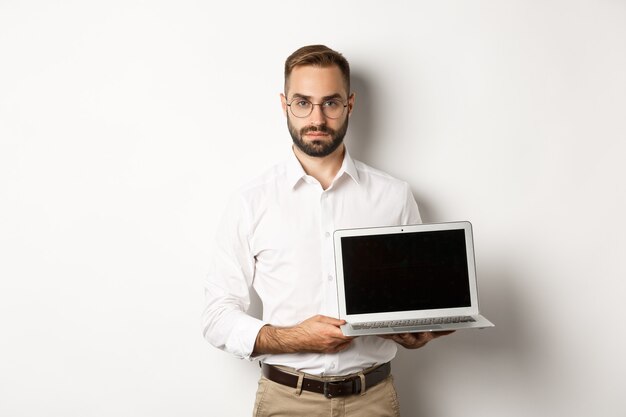 Selbstbewusster Manager, der Präsentation auf dem Bildschirm demonstriert, Laptop-Anzeige zeigt und ernst steht, stehend