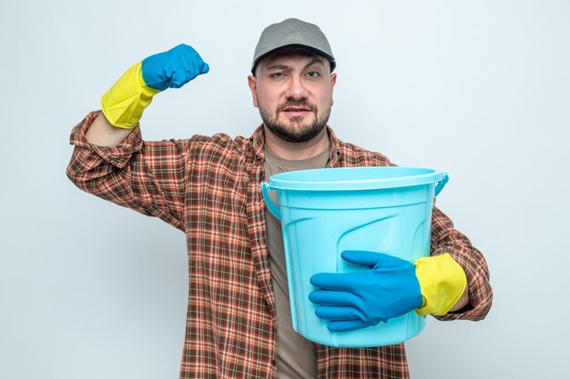 Selbstbewusster slawischer Putzmann mit Gummihandschuhen, der einen Eimer hält und die Faust hochhebt