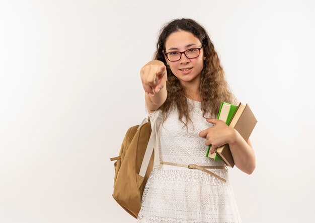 Selbstbewusstes junges hübsches Schulmädchen, das Brille und Rückentasche hält Bücher hält, die lokal auf Weiß mit Kopienraum zeigen