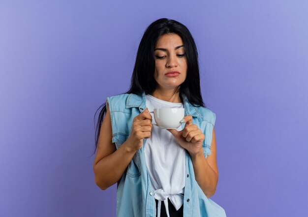 Selbstbewusstes junges kaukasisches Mädchen hält und schaut Tasse an