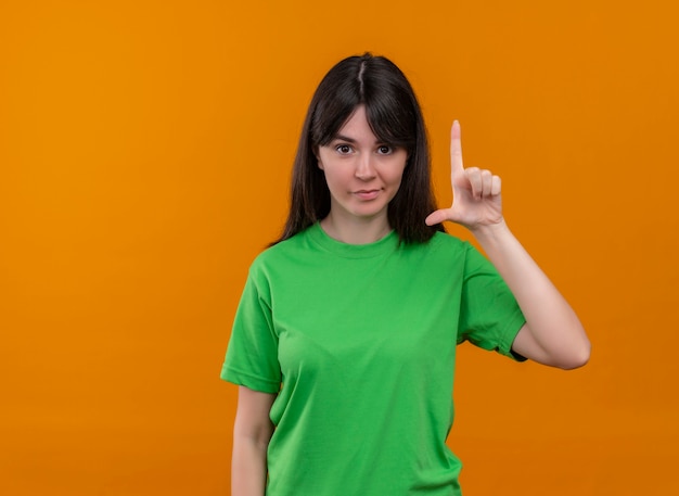 Selbstbewusstes junges kaukasisches Mädchen im grünen Hemd zeigt Handrücken, der auf lokalem orange Hintergrund nach oben zeigt