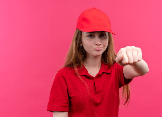 Selbstbewusstes junges Liefermädchen in roter Uniform, die ihre Faust auf isoliertem rosa Raum mit Kopienraum ausstreckt