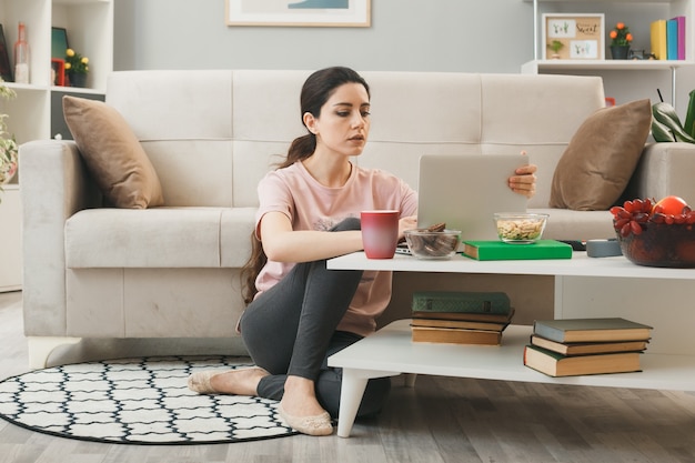 Selbstbewusstes junges Mädchen benutzte Laptop auf dem Boden hinter dem Couchtisch im Wohnzimmer?