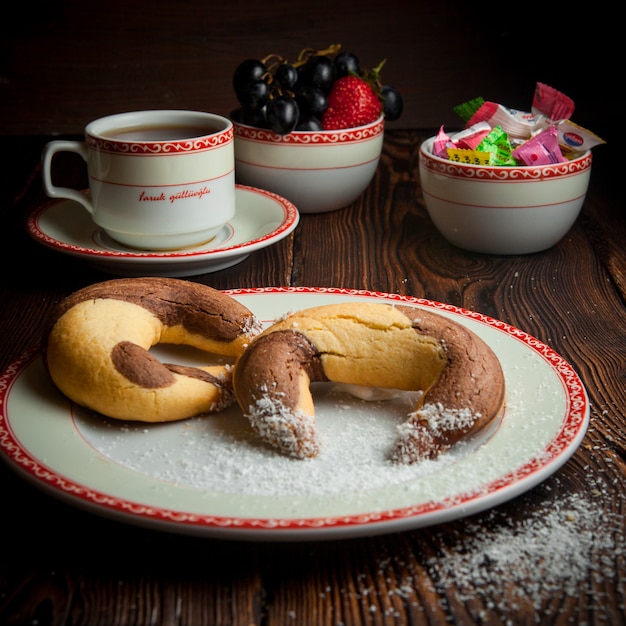Selbstgemachte Kekse der Nahaufnahme mit Tasse Tee und Süßigkeiten auf Holztisch