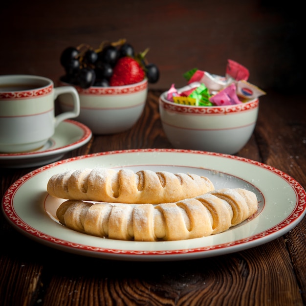 Selbstgemachte Kekse der Seitenansicht-Nahaufnahme mit Tasse Tee, Süßigkeiten und Beeren auf Holztisch