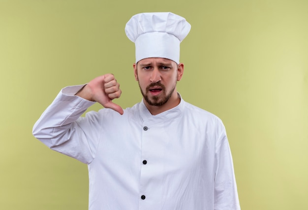 Kostenloses Foto selbstzufriedener professioneller männlicher koch kocht in der weißen uniform und im kochhut, der auf sich zeigt, der über grünem hintergrund steht