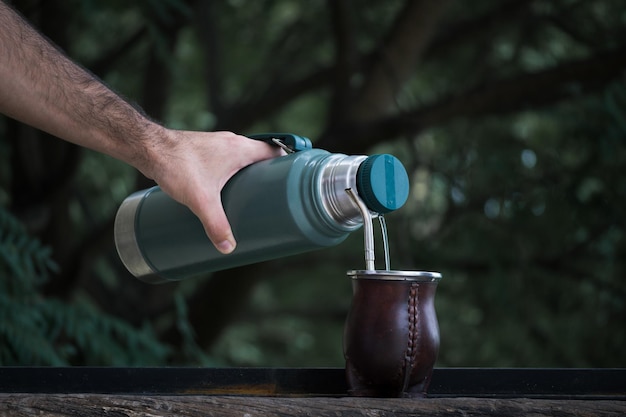 Selektive Fokusaufnahme einer Hand, die Wasser aus einer Thermoskanne in eine Tasse gießt