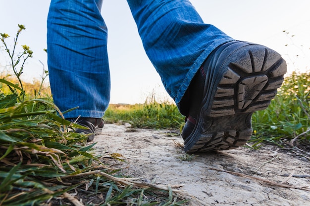 Selektive Fokusaufnahme von Füßen eines Wanderers in Stiefeln, der einen Weg am Stadtrand entlang geht