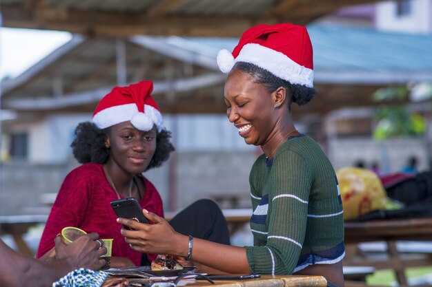 Selektive Fokusaufnahme von schönen schwarzen Frauen, die Weihnachtsmützen tragen und auf ein Handy schauen