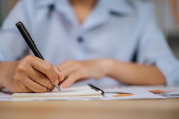 Selektive Fokushand einer asiatischen jungen Frau in Brillen verwendet einen Stift, der im Homeoffice mit Papieren arbeitet, während der Quarantäne-Kovid-19-Selbstisolation zu Hause, das Konzept der Arbeit von zu Hause aus