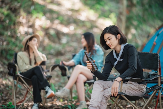 Selektive Fokussierung schöne asiatische Frau und Freunde Reisende entspannen sich vor dem Campingzelt Sie genießen es, mit Spaß und Freude zusammen zu reden und Bier zu trinken