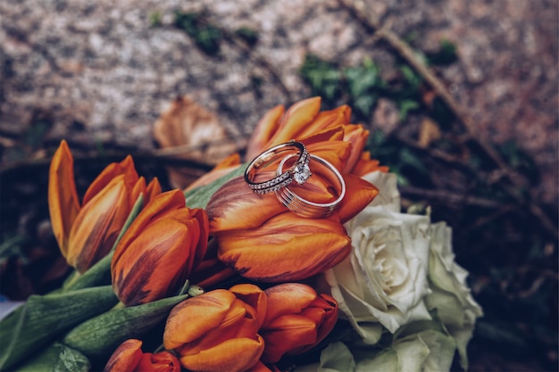 Kostenloses Foto selektive nahaufnahme von silbernen diamantringen auf orangefarbenen tulpen und weißen rosen