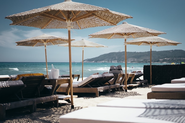 Kostenloses Foto selektive weitwinkelaufnahme von braunen holzliegen unter sonnenschirmen am strand