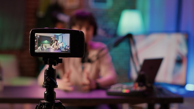 Selektiver Fokus auf den Bildschirm der digitalen Videokamera, der den Inhaltsersteller aufzeichnet, der Live-Internetradio mit dem Mikrofon aus dem Heimstudio streamt. Influencer-kaukasische Frau, die Vlog für Social-Media-Beiträge filmt.