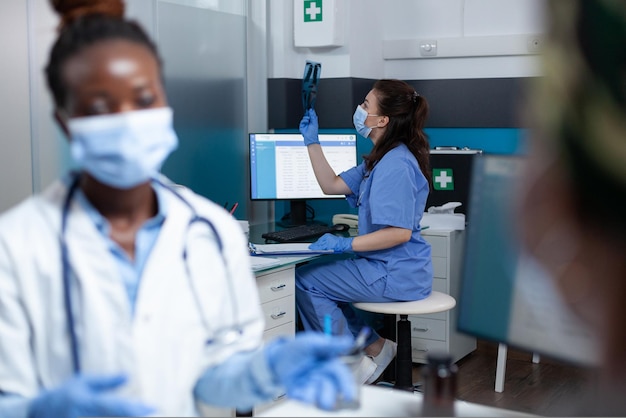 Selektiver Fokus auf die medizinische Krankenschwester, die die Lungenradiographie während der klinischen Untersuchung im Krankenhausbüro analysiert. Afroamerikaner mit Gesichtsmaske gegen Coronavirus, der Krankheitssymptome erklärt