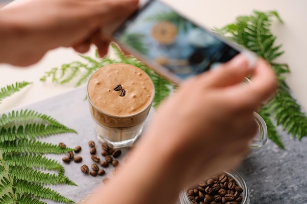 Selektiver Fokus Frauenhände machen per Telefon ein Bild für soziale Medien trendiges, flauschiges koreanisches Getränk mit Schlagsahne Dalgona-Kaffee mit Mandelmilch auf Marmorplatte