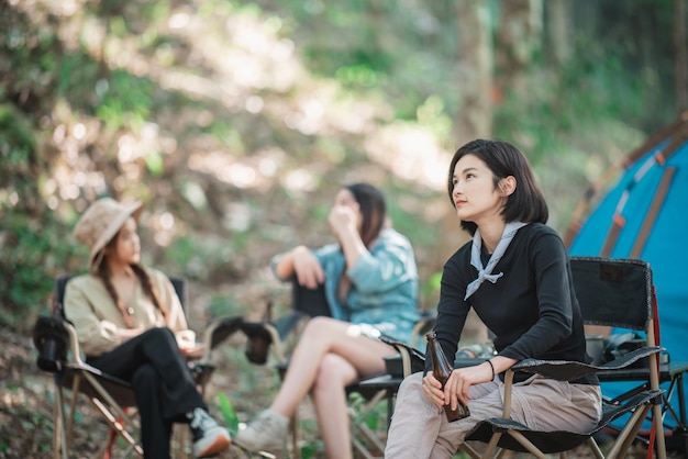 Selektiver Fokus Junge asiatische hübsche Frau und ihre Freundin, die vor dem Zelt sitzen, benutzen das Handy, um beim Camping im Wald mit Glück zusammen zu fotografieren