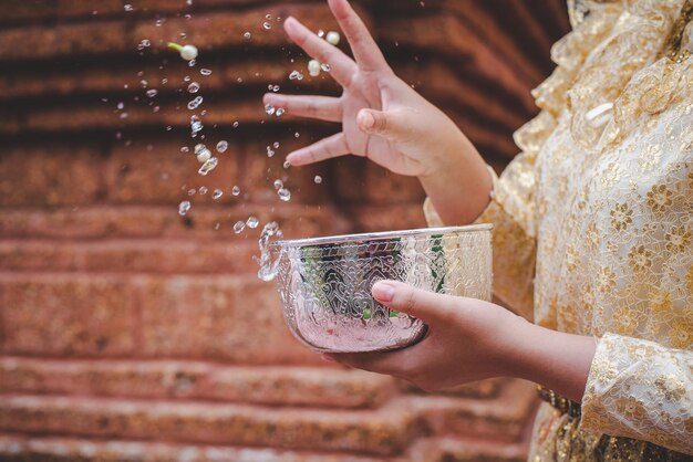 Selektiver Fokus und Nahaufnahme Weibliche Hand, die Wasserschüssel hält und Wasser in Tempeln spritzt und die gute Kultur der Thailänder während des Songkran-Festivals bewahrt Thai-Neujahrs-Familientag im April