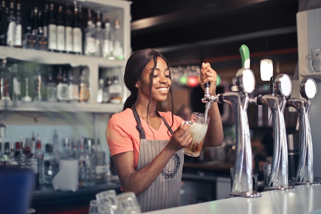 Selektiver Fokusschuss einer afroamerikanischen Barkeeperin, die Bier aus einer Barpumpe füllt